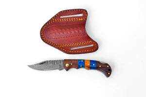 A Damascus steel folding pocket knife with a brown and blue handle, alongside a hand-stitched leather sheath.